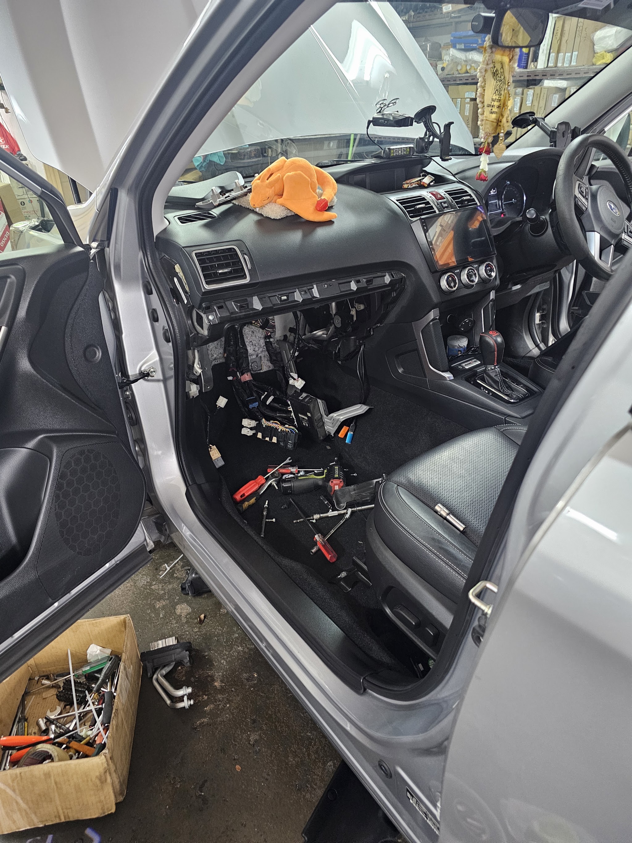 A silver car with its entire dashboard removed and the wiring loom exposed, tools laid out on the floor mat